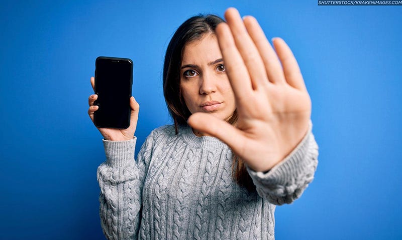 Photo of a woman holding a mobile phone in one hand and holding up her other hand in a "stop" gesture