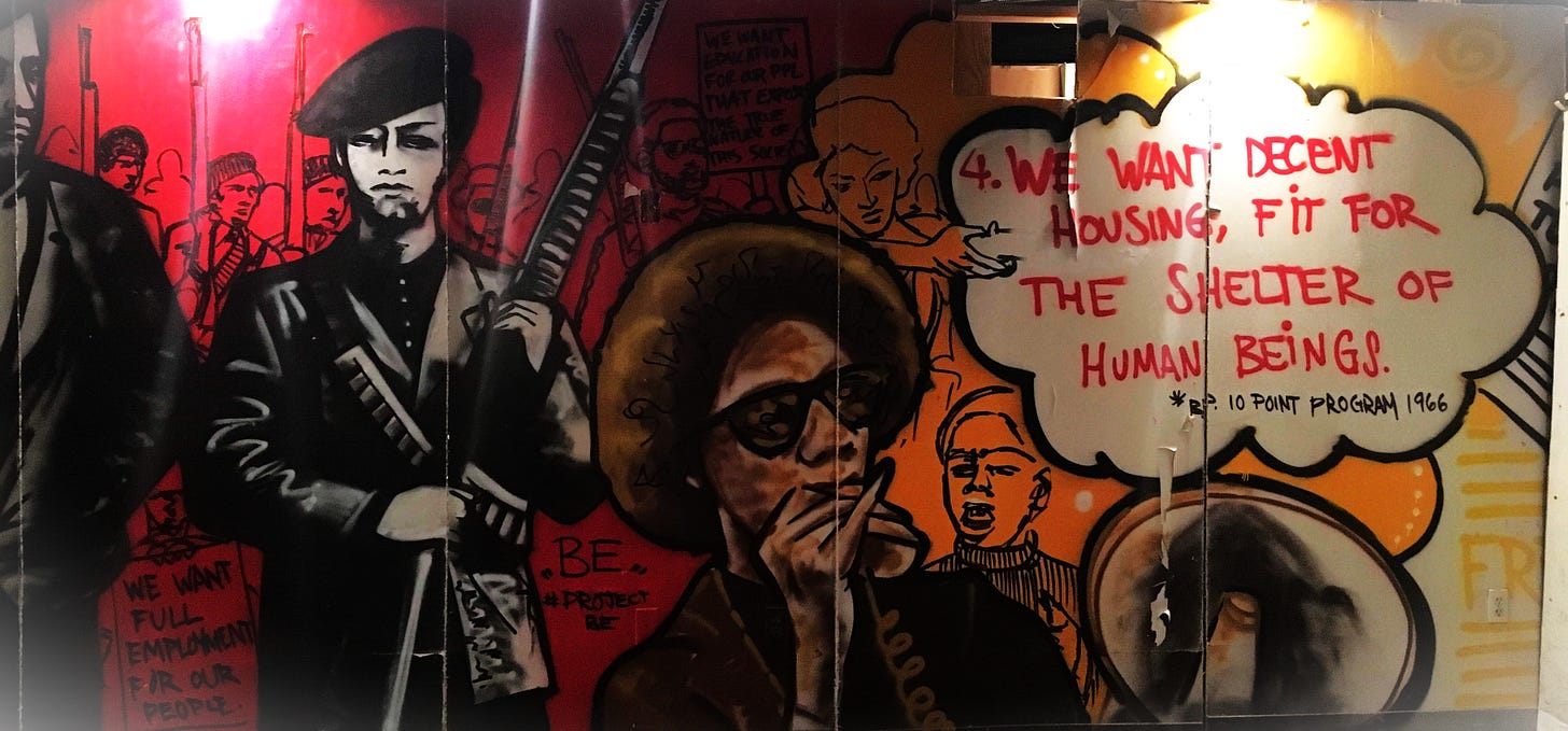 Mural of a Black Panther Party member with a megaphone, two members standing behind them, and a large crown of members in the background holding signs corresponding to the 10-point program. The most prominent reads: "4. We want decent housing for the shelter of human beings"