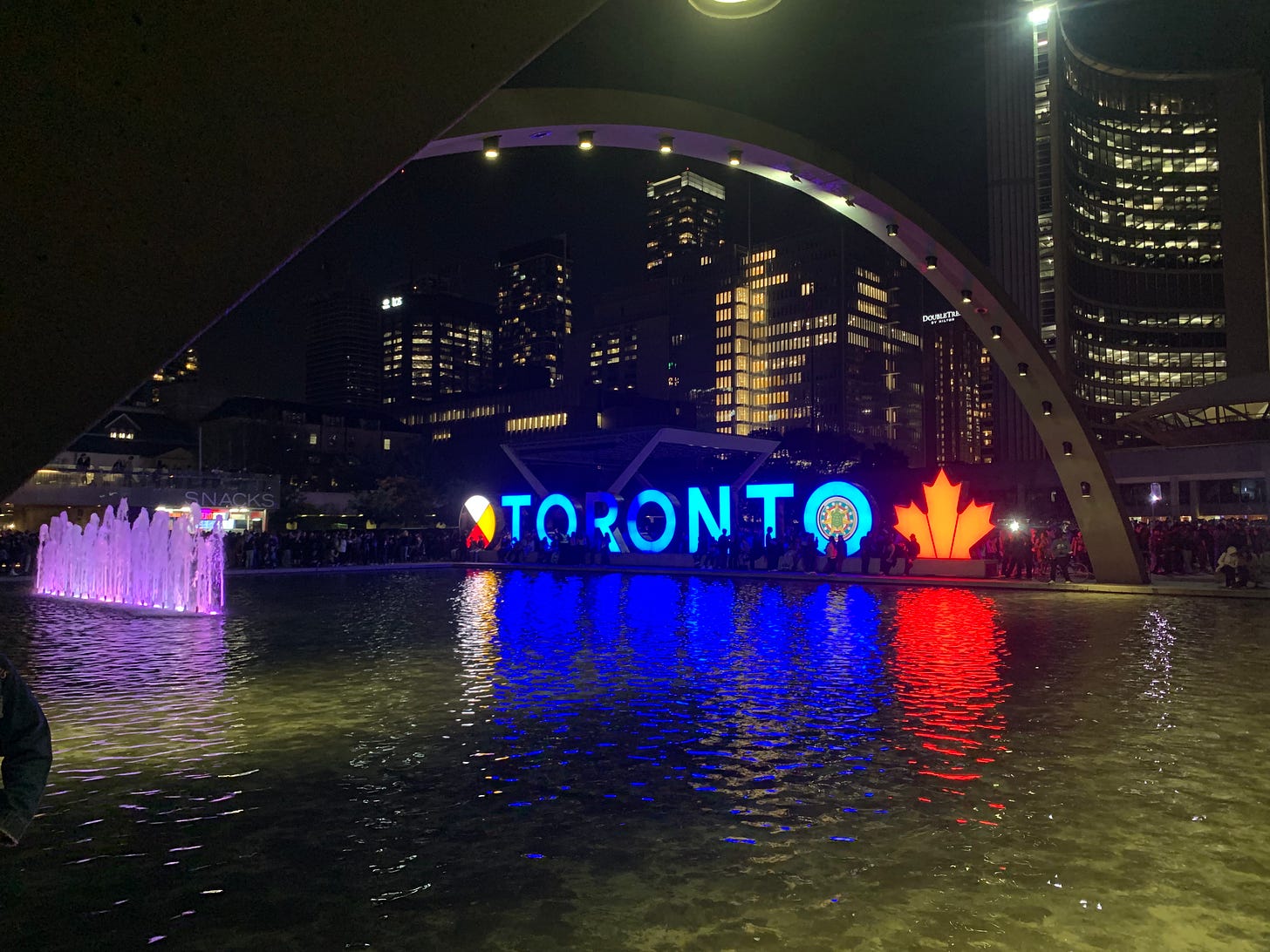 A square public fountain with the words TORONTO lit up in blue.
