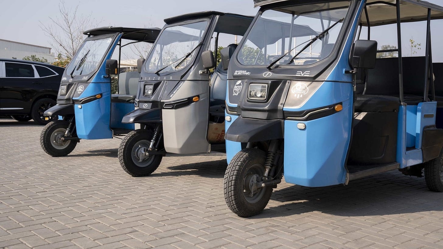 Three colorful electric auto rickshaws parked side by side on a paved surface.