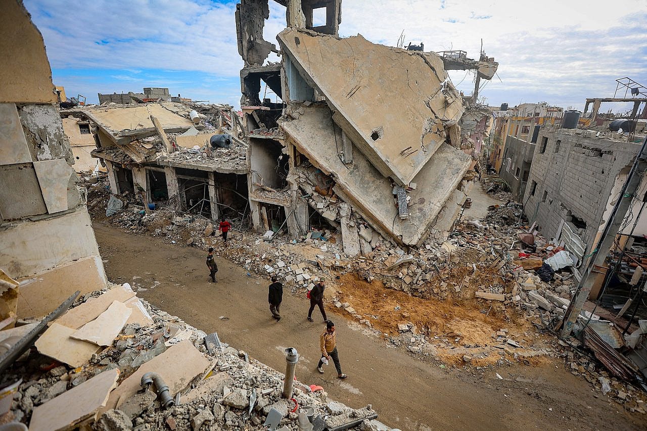 Palestinians walk next to the rubble of buildings destroyed by Israeli airstrikes in Khan Younis, southern Gaza Strip, November 28, 2023. (Atia Mohammed/Flash90)