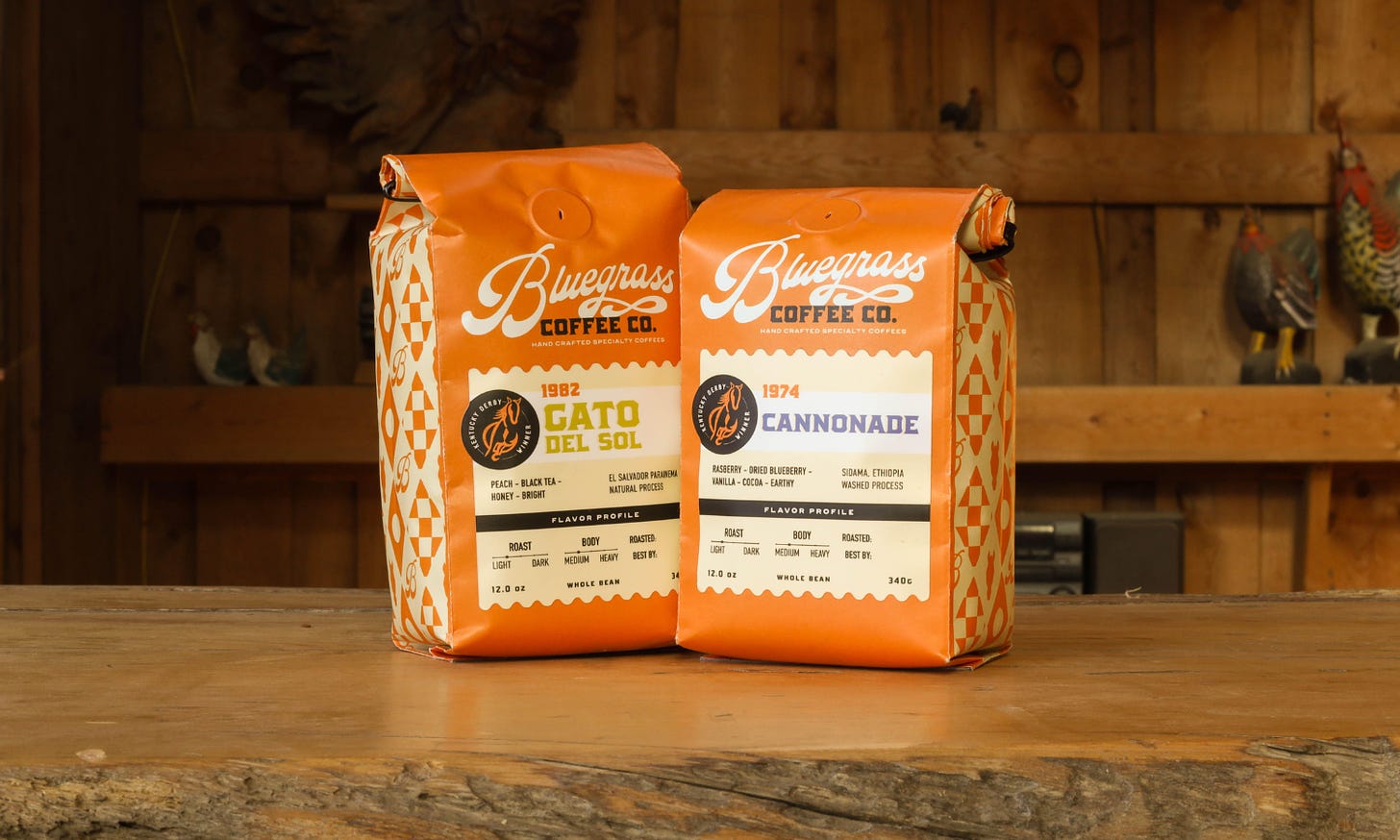 Close-up of two mostly orange coffee bags on a wooden table. The informative labels are in an off-white tinted orange with grey and black text.