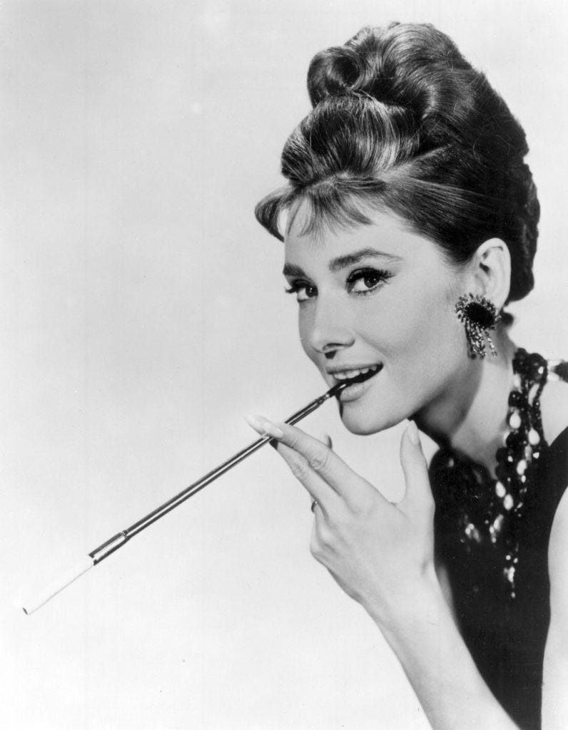 A black and white image of Hepburn, looking impossibly glamorous as Holly Golightly, smoking a cigarette in a long holder