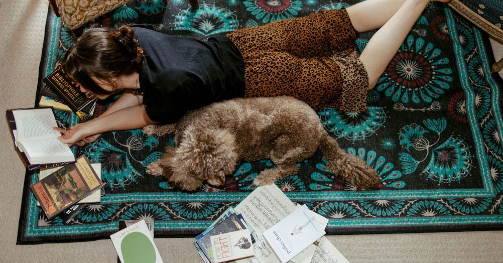 Linea laying on the floor reading surrounded by books and her dog