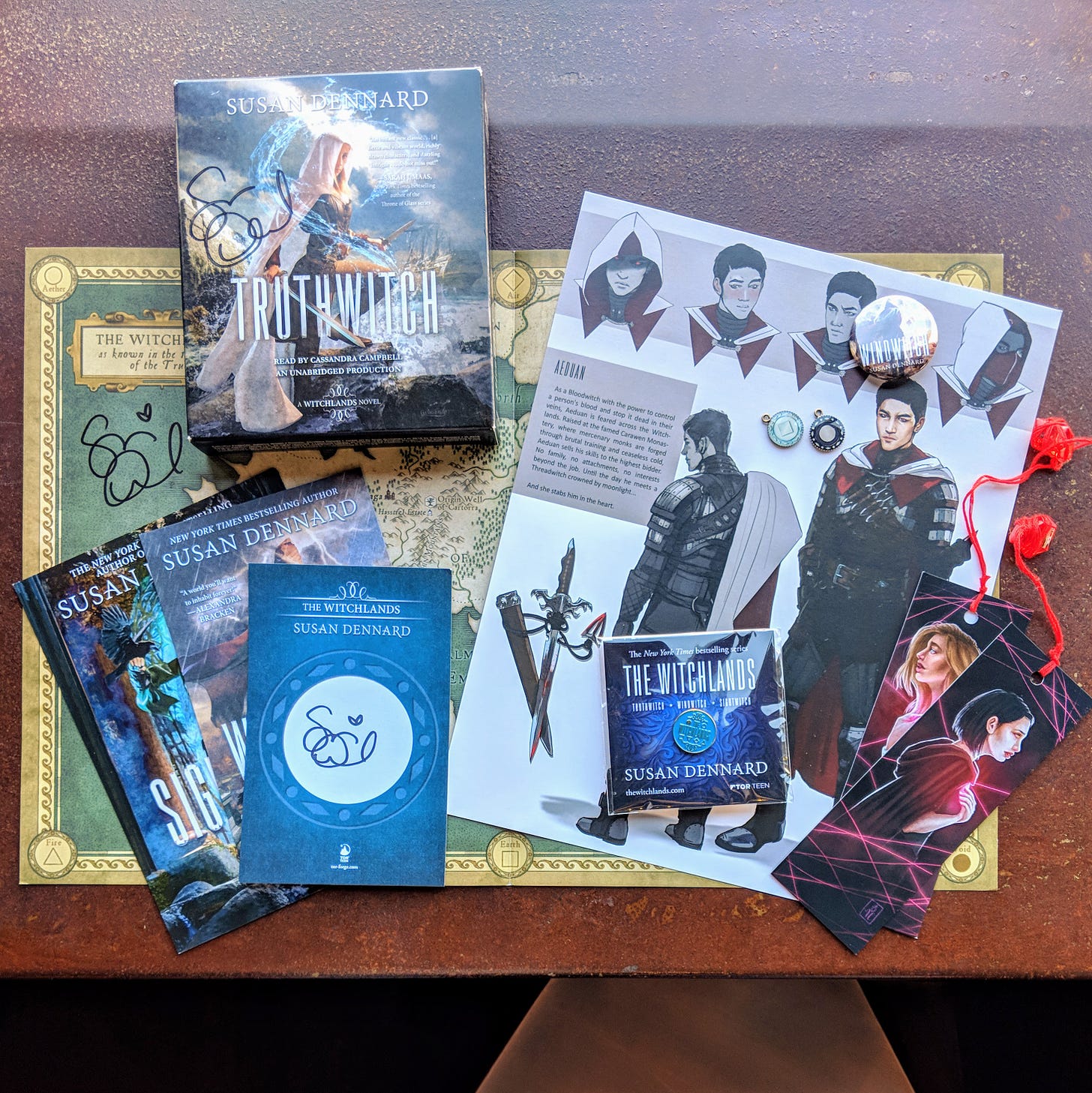 Examples of Witchlands swag including bookmarks, post cards, book plates, buttons, pins, charms, posters, and maps
