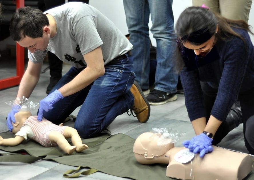 A man on the left and a woman on the right practice CPR on a dummy infant and an adult dummy respectively, showcasing lifesaving skills in emergency response training.