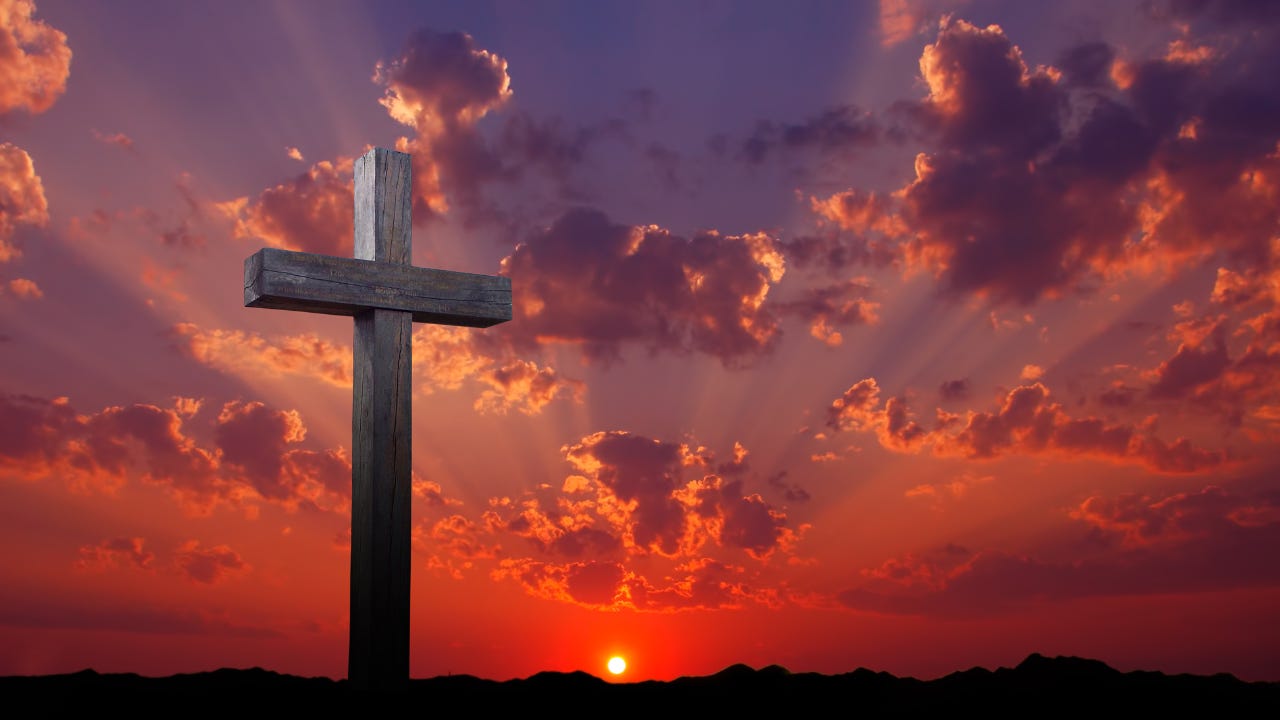 A wooden cross in front of the setting sun.