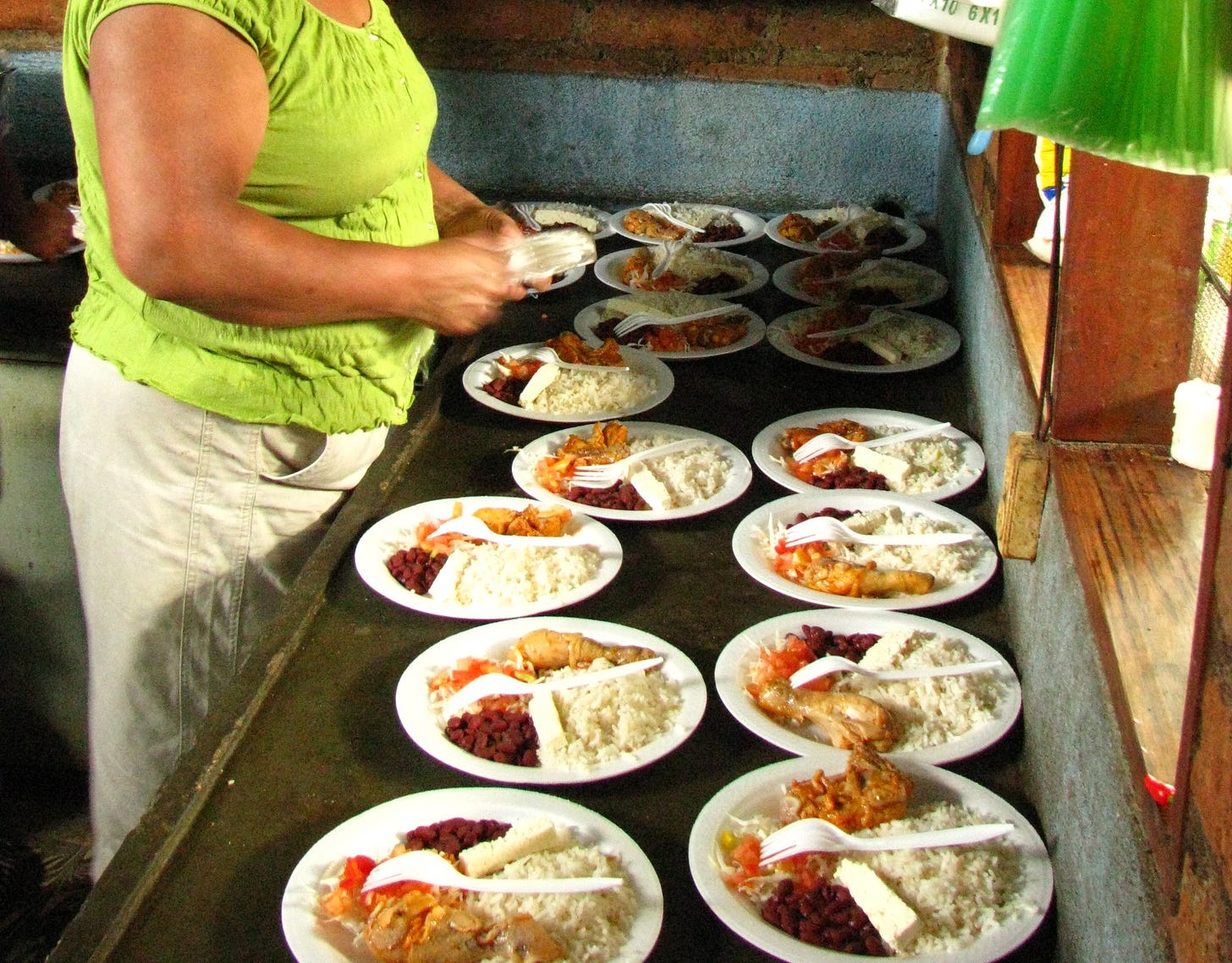 In this picture you can see multiple plates ready to serve with the same serving of rice, beans, white cheese and fried chicken - there is a lady standing over them making the final touches to the plates.