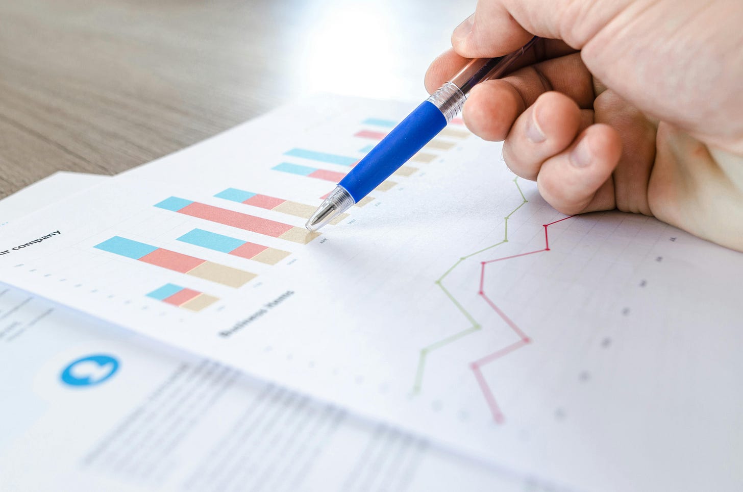 A person holding a blue and silver pen reviews a page with colourful bar graphs and other data.