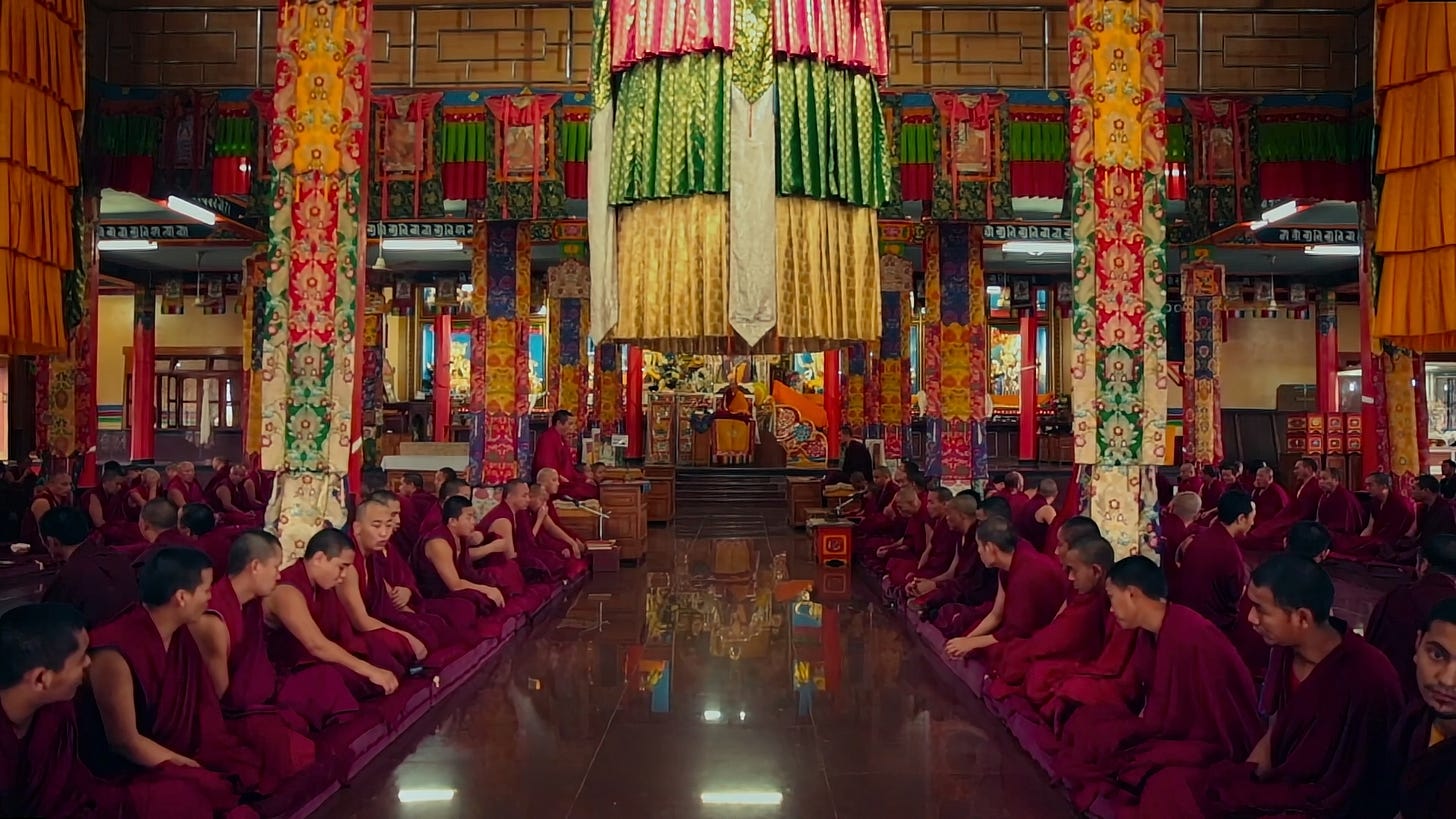 Photo of monks in red robes sitting in colorfully decorated temple.