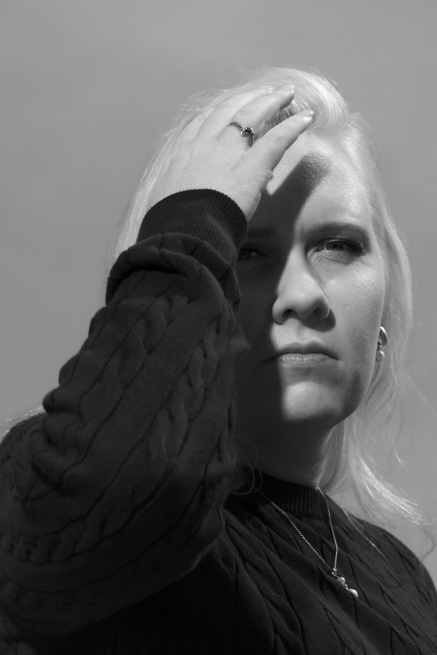 A blackandwhite photo of a blonde person with their hand raised to their forehead.