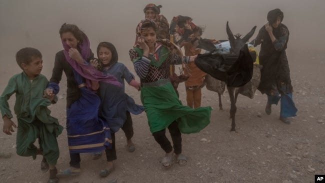 Afghan girls and women carry donated aid to their tents during a fierce sandstorm after the earthquake in Zendah Jan district in Herat Province in October 2023.