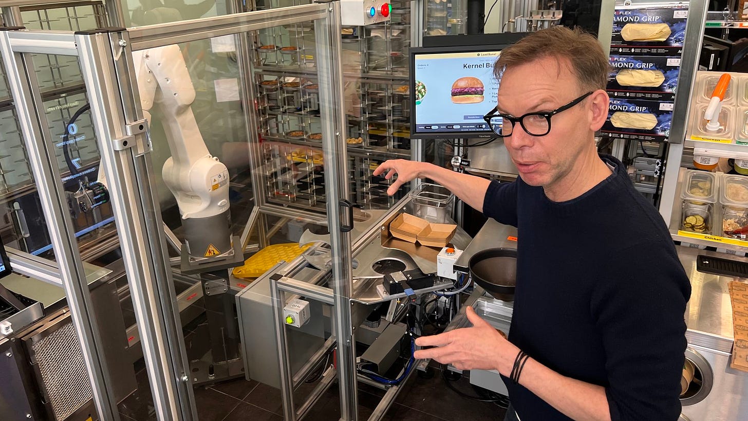 Steve Ells, the founder of Chipotle, next to a robotic arm in a restaurant.