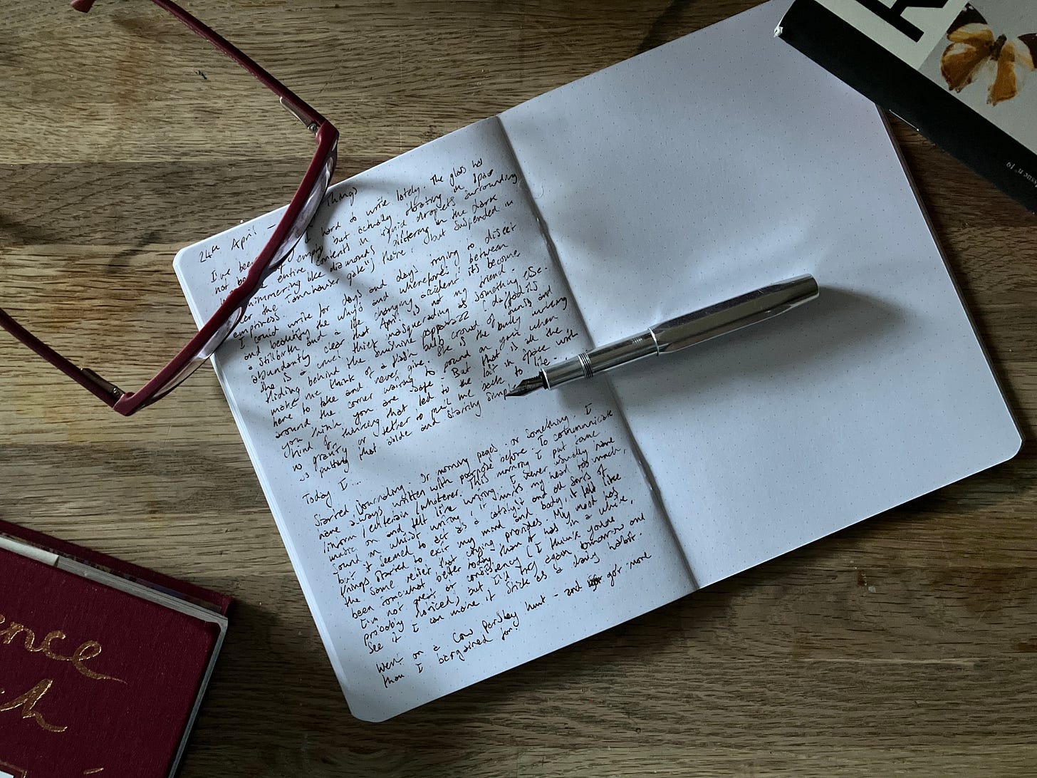 An half written journal lies atop a table with a pair of spectacles and a fountain pen resting on it