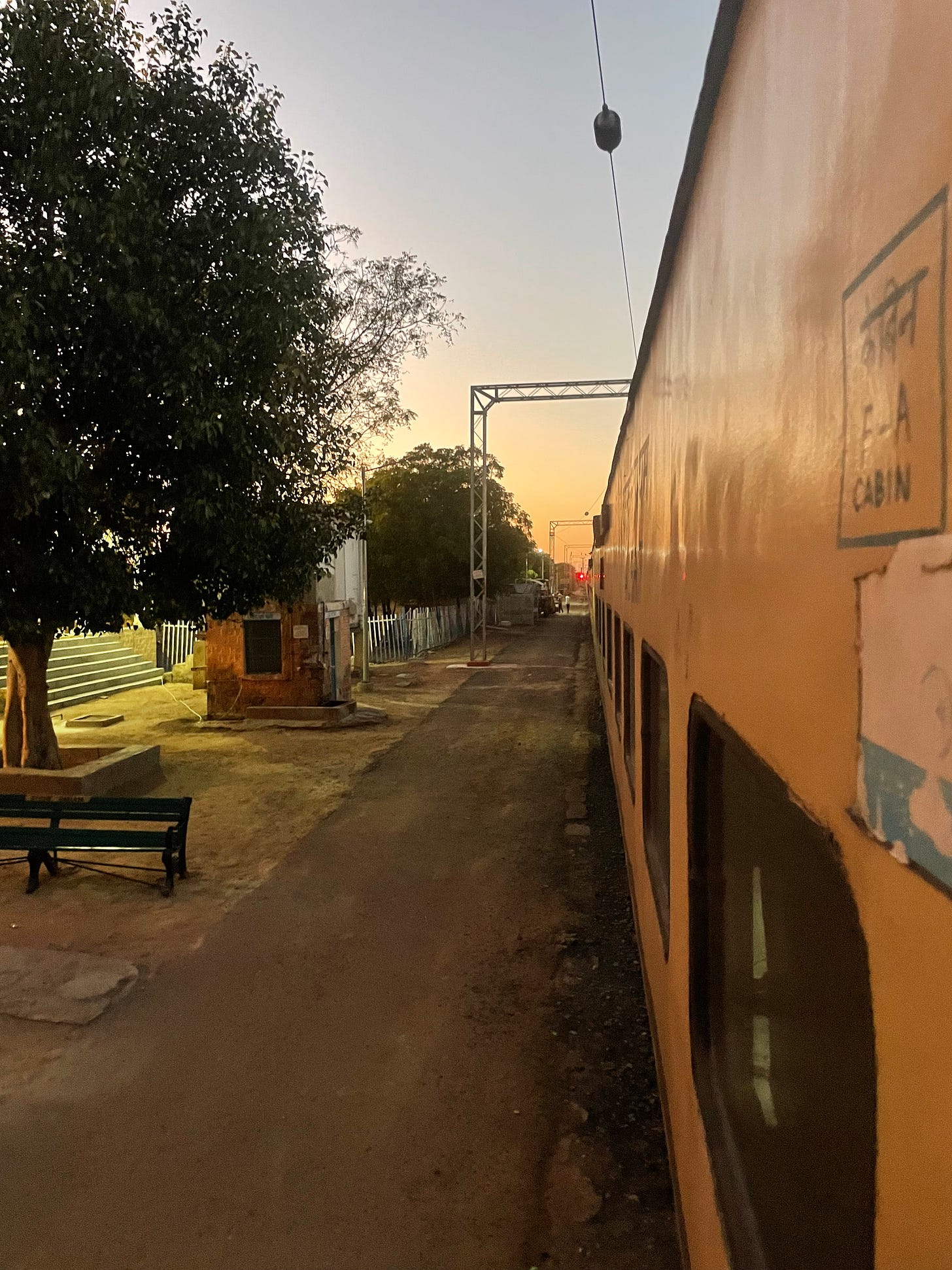 A view down the long side of an yellow train car at sunset. Indian writing near the door reads, in Hindi and English, "F-A Cabin"