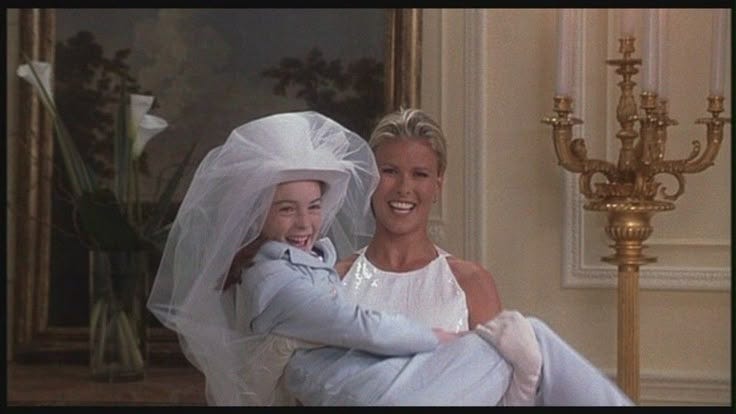This may contain: two women in white dresses and veils are hugging each other while sitting on a chair