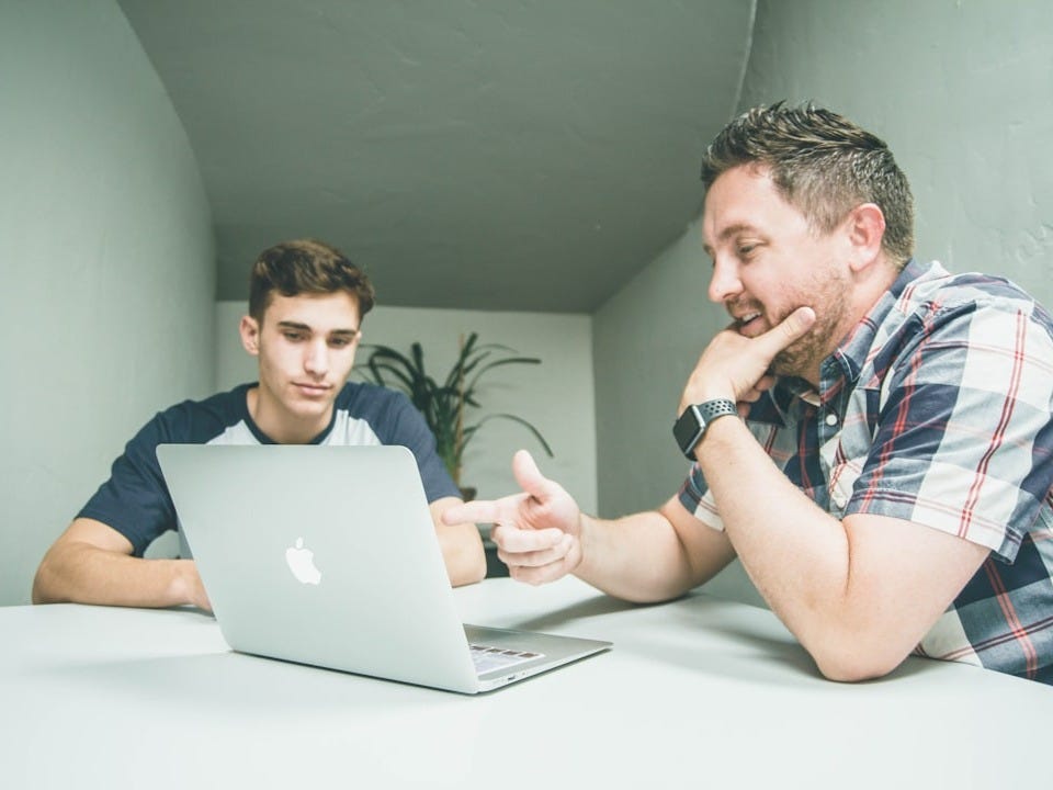 man wearing white and black plaid button-up sports shirt pointing the silver MacBook