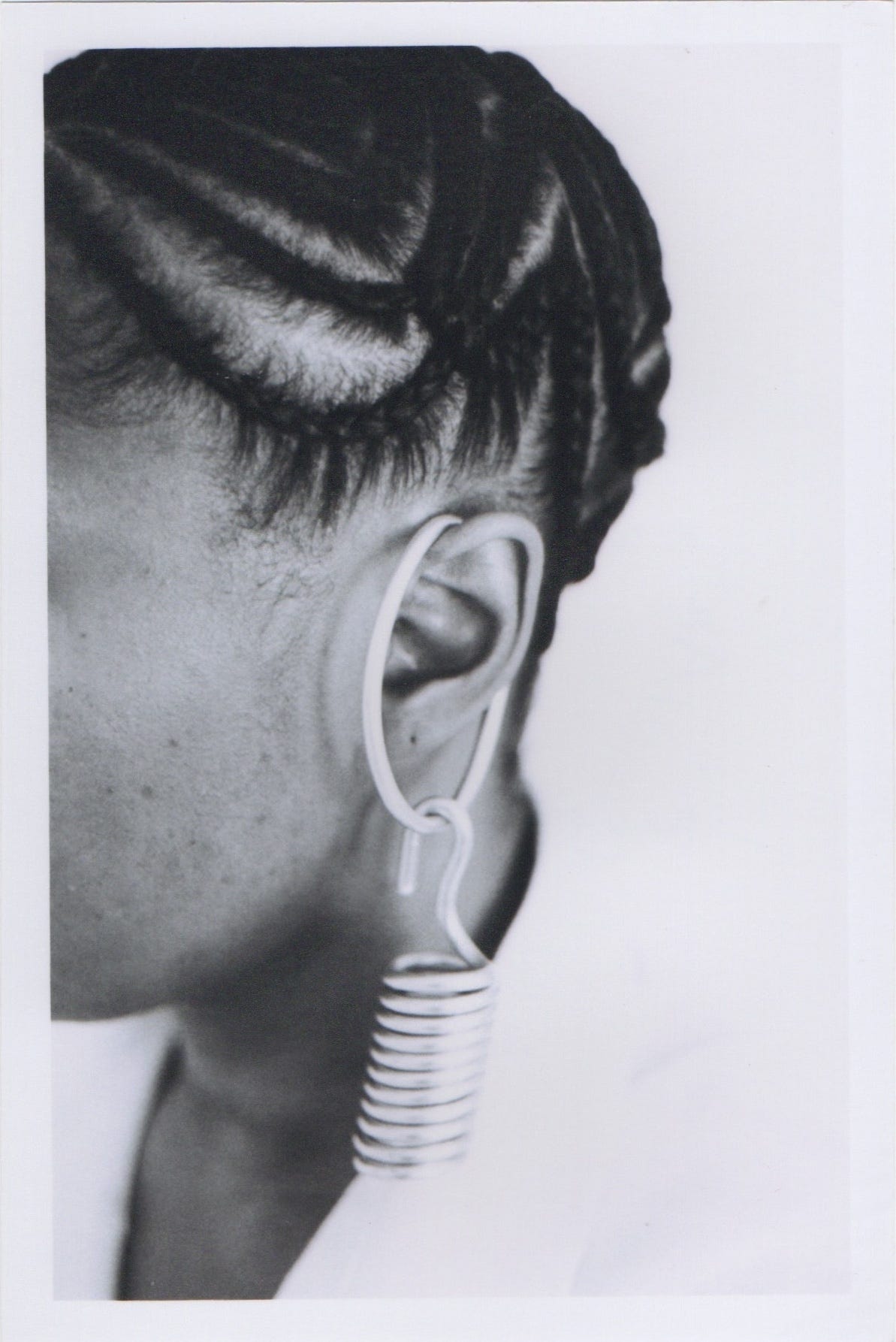 Black and white photograph of cryptographic cornrows and a coiled Cykofian artifact made of alumninum wire hanging from a pierced ear. 