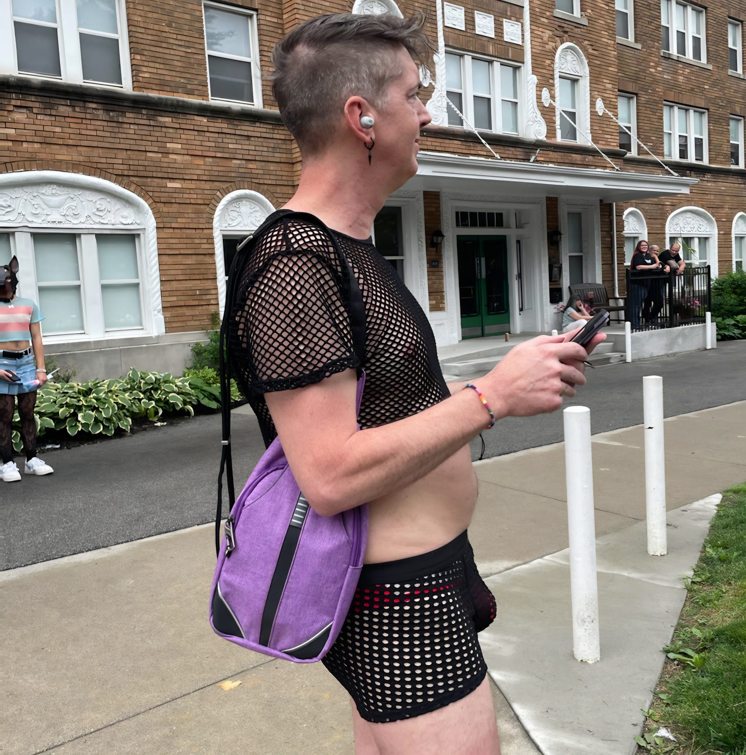 author wearing mesh shirt and mesh shorts holding a phone with a small satchel 