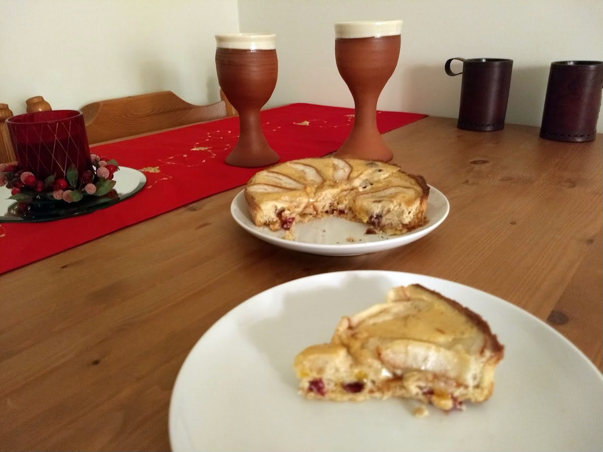 A pie with a slide cut out and served on a plate, set on a wooden table with mugs and a centrepiece.