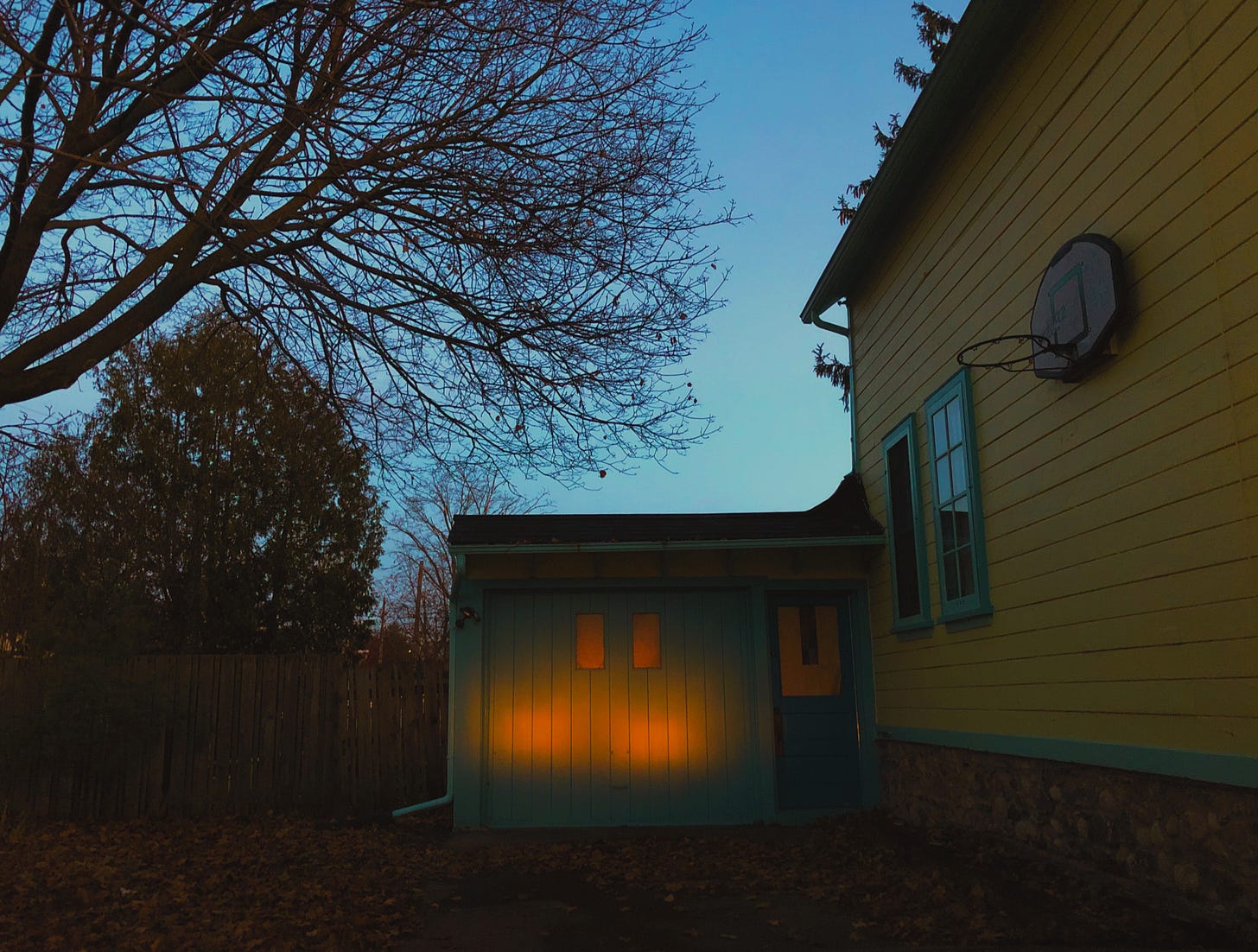 Headlights on a garage door at dusk as a car backs out of a driveway. Photo credit: Nancy Forde. All rights reserved. nancyforde.com