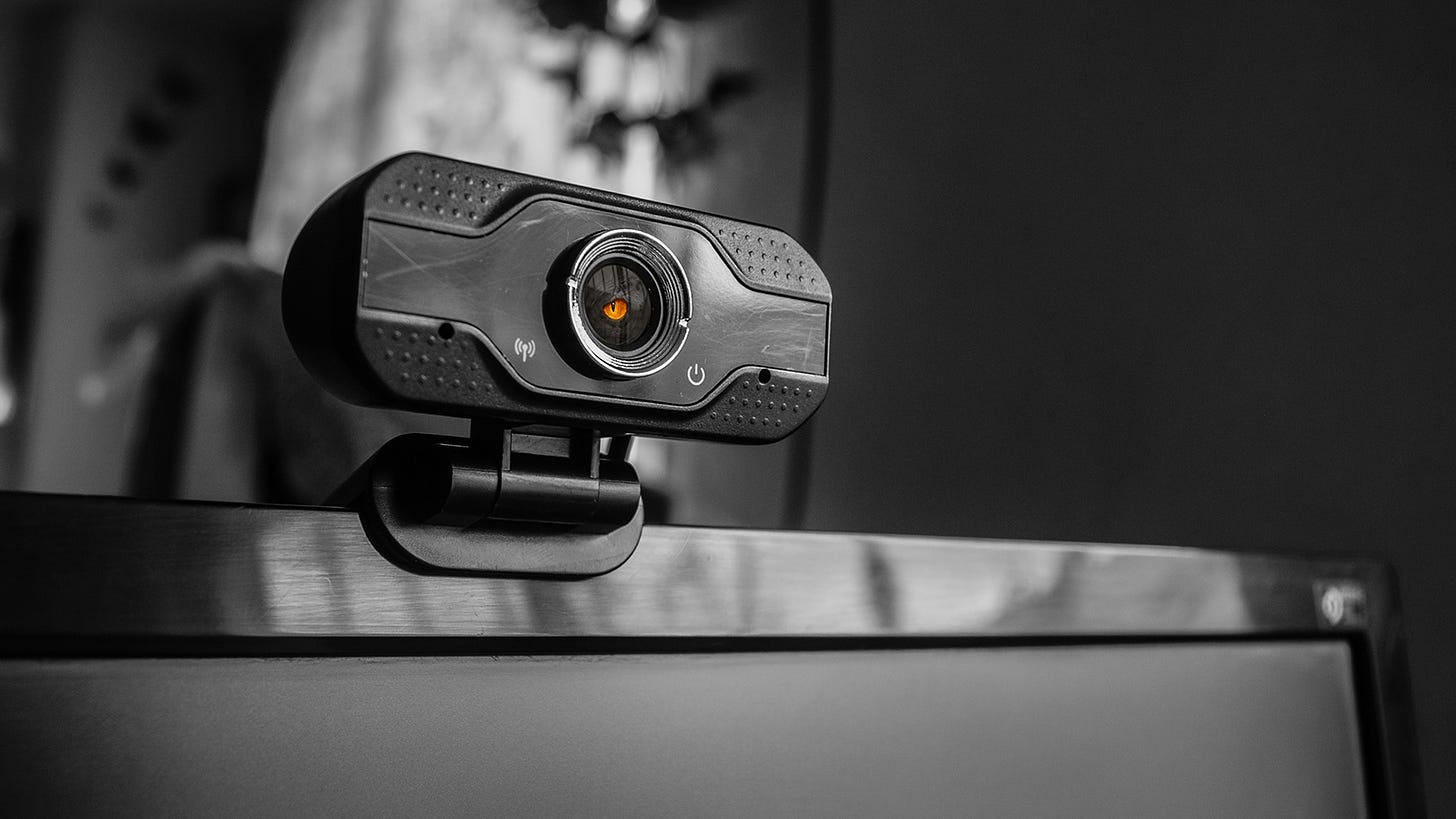 An external computer camera perches on a screen with a yellow dragon eye in its lens