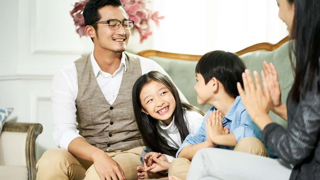 Young asian parents and two children sitting on couch chatting in family living room at home