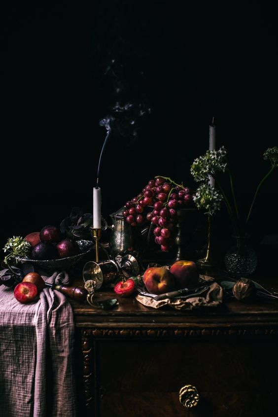 Dutch Golden Age Inspired Still Life by Betty Shin Binon shows a dark but lush table laden with fruits and tapered candles recently extinguished and their smoke spirals upwards.