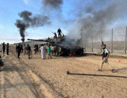 Members of the Ezz Al-Din Al Qassam Brigades, the military wing of Hamas, burn an Israeli military armored vehicle outside the Gaza Strip, October 7, 2023. (Photo: Stringer/APA Images)