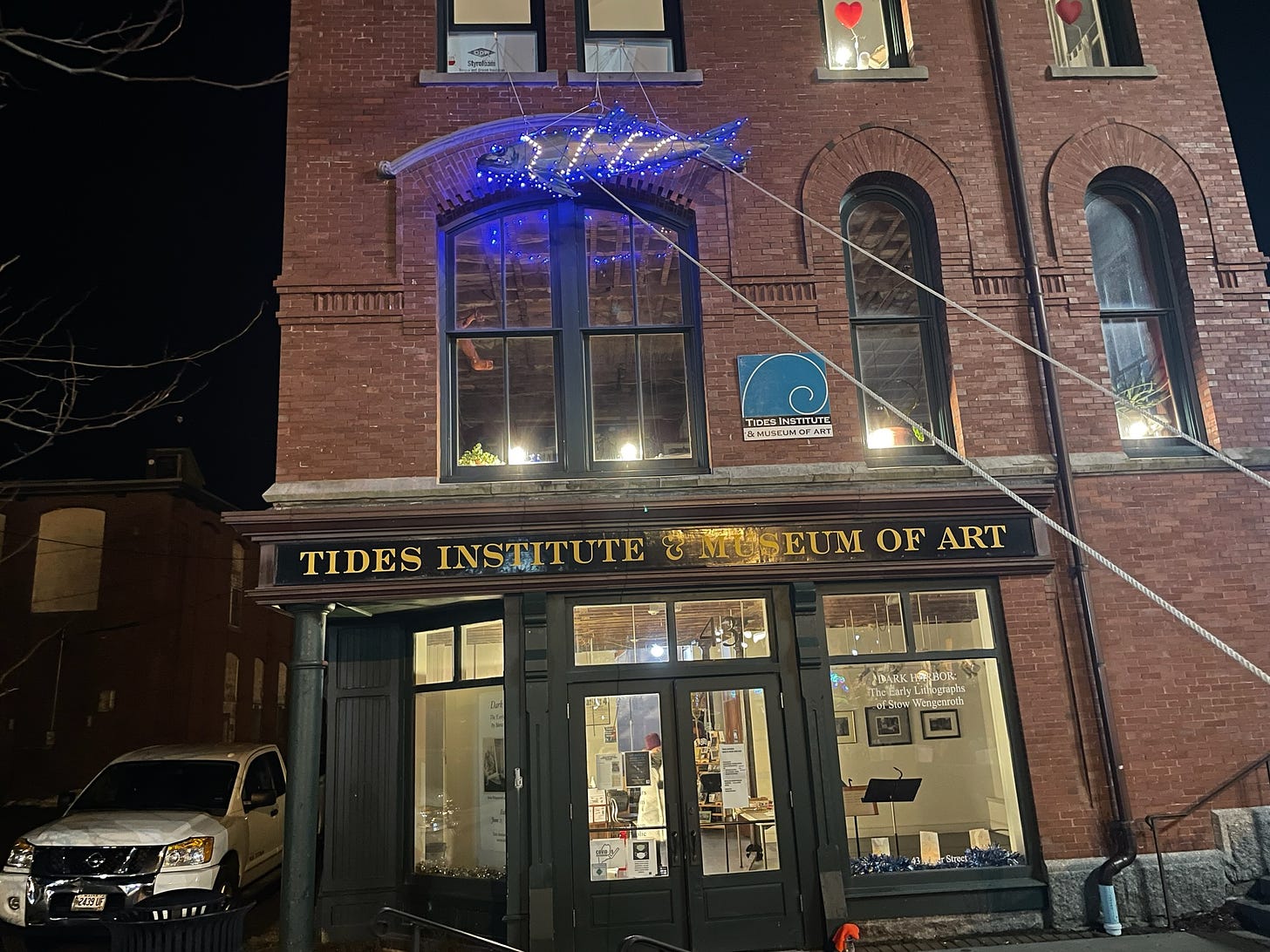 A cutout of a sardine is being hoisted up to the second story of a brick building that is the Tides Institute and Museum of Art