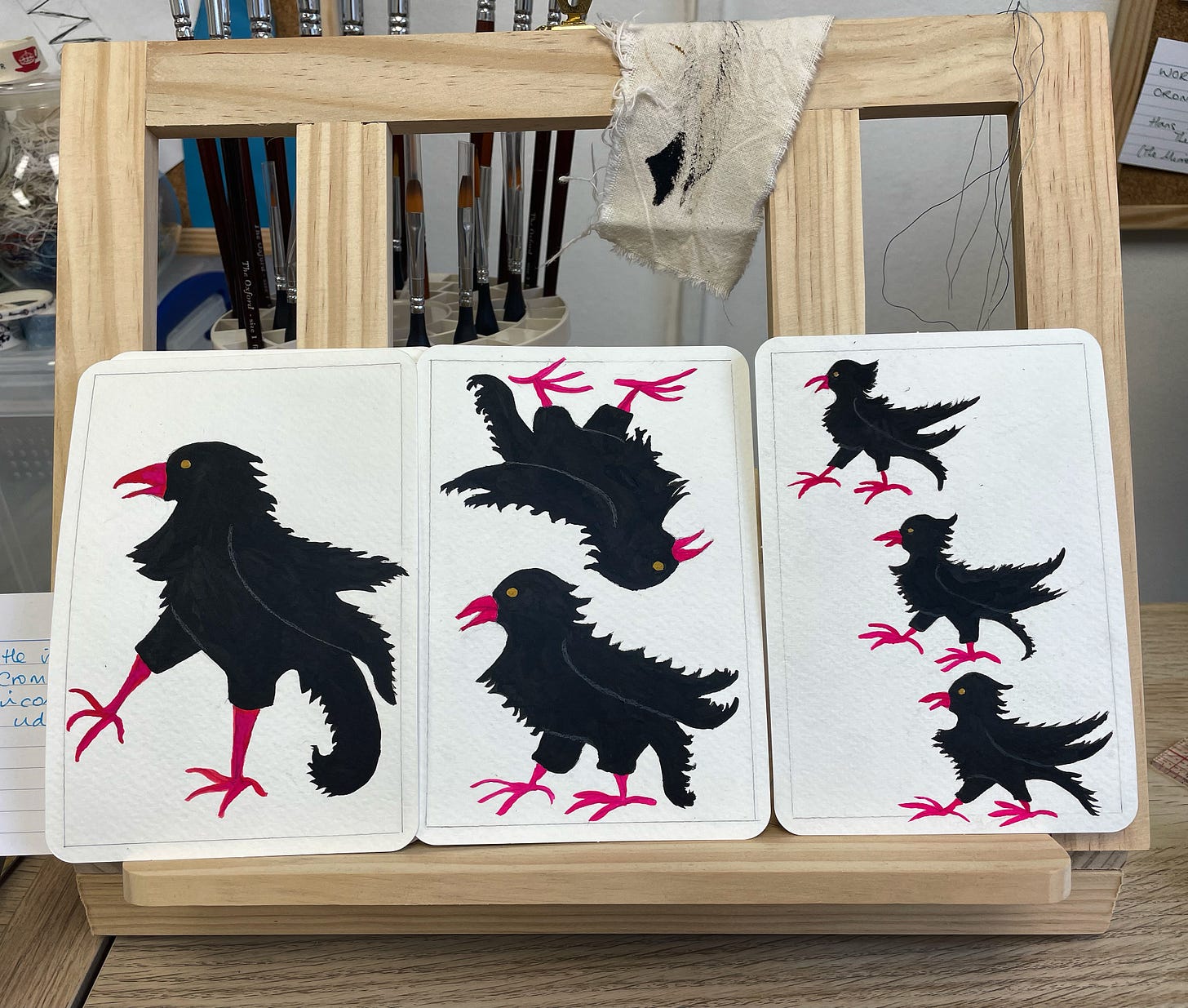 Three playing cards featuring one, two, and three Cornish choughs, resting on a wooden stand.