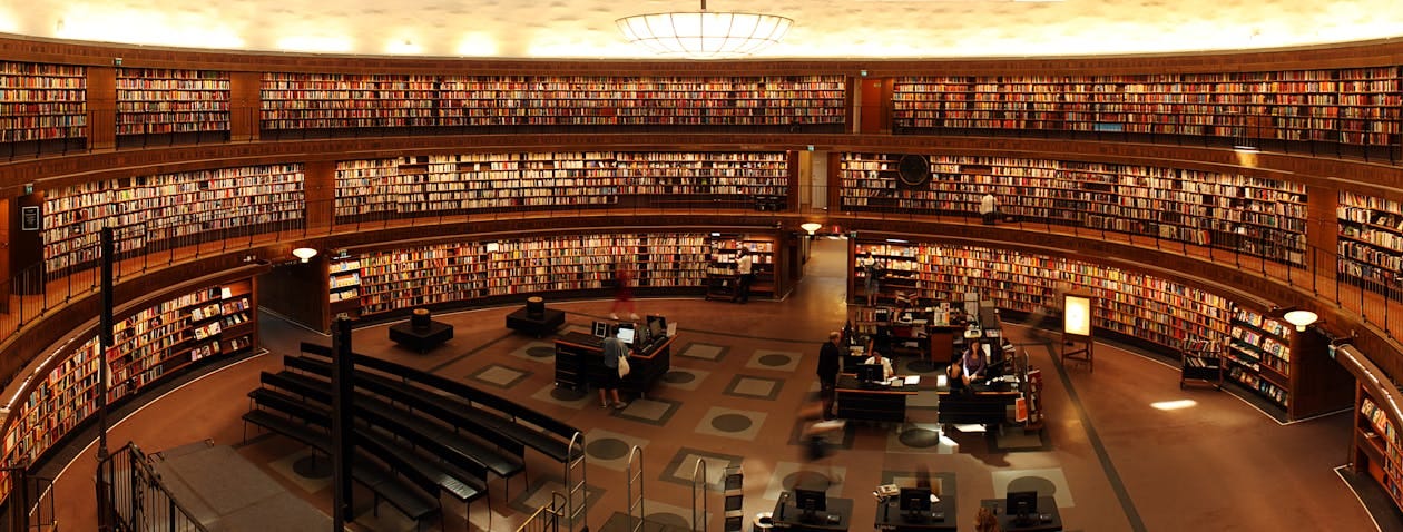 Free Panoramic view of a grand circular library with shelves full of books and study desks. Stock Photo