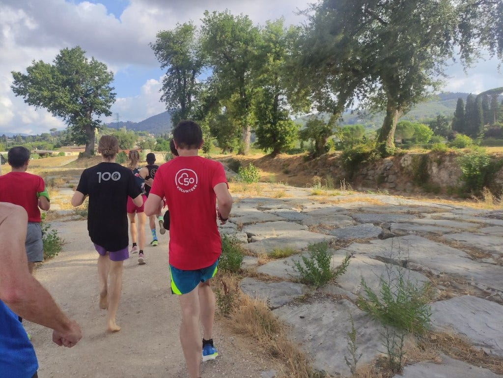 Runners in parkrun shirts head off along a gravelled path, with one running barefoot