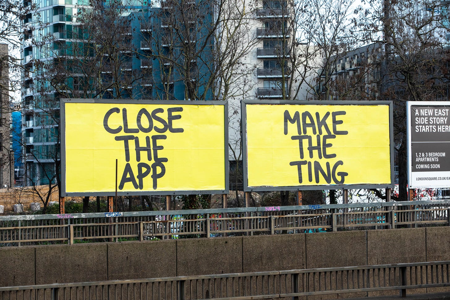 Image shows two yellow billboards reading "CLOSE THE APP" and "MAKE THE TING".