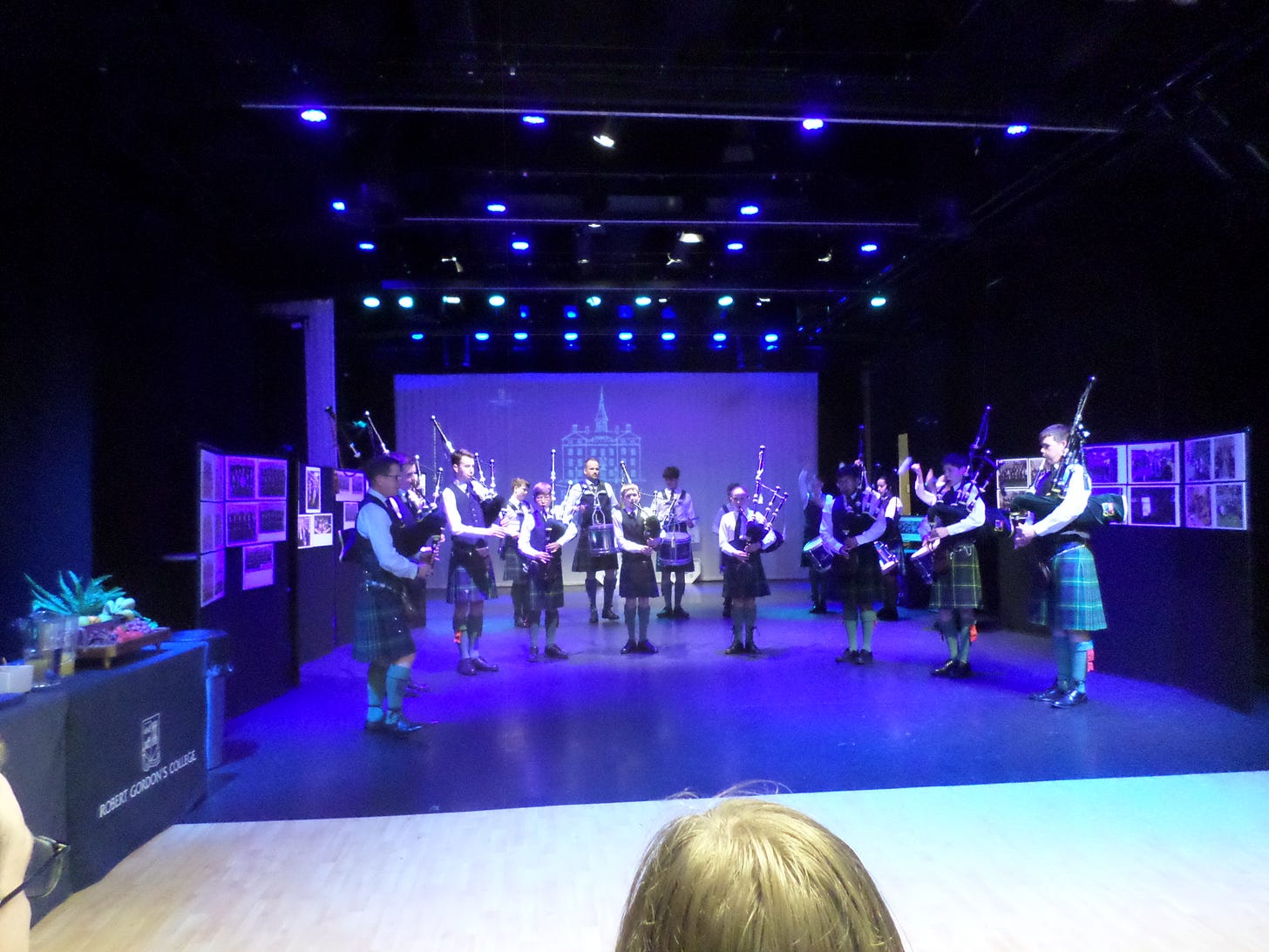 A number of bagpipers standing on a blue stage
