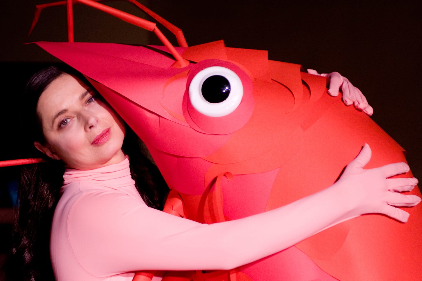 Isabella Rossellini embracing a shrimp constructed out of paper.