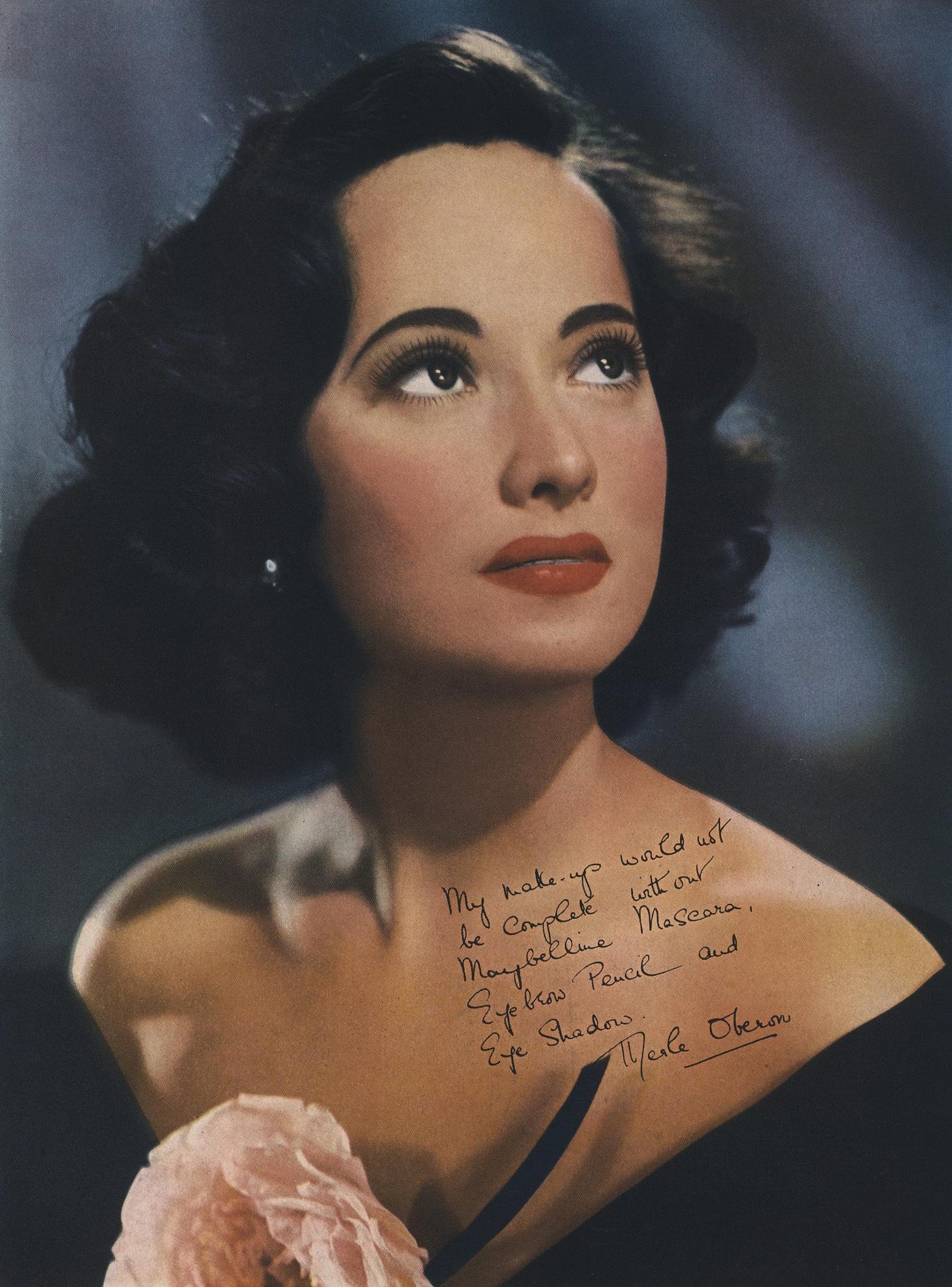 color photo of Merle Oberon looking up, bare shoulders in a plunging black dress, red lipstick, with a short note written and signed in her hand on the image