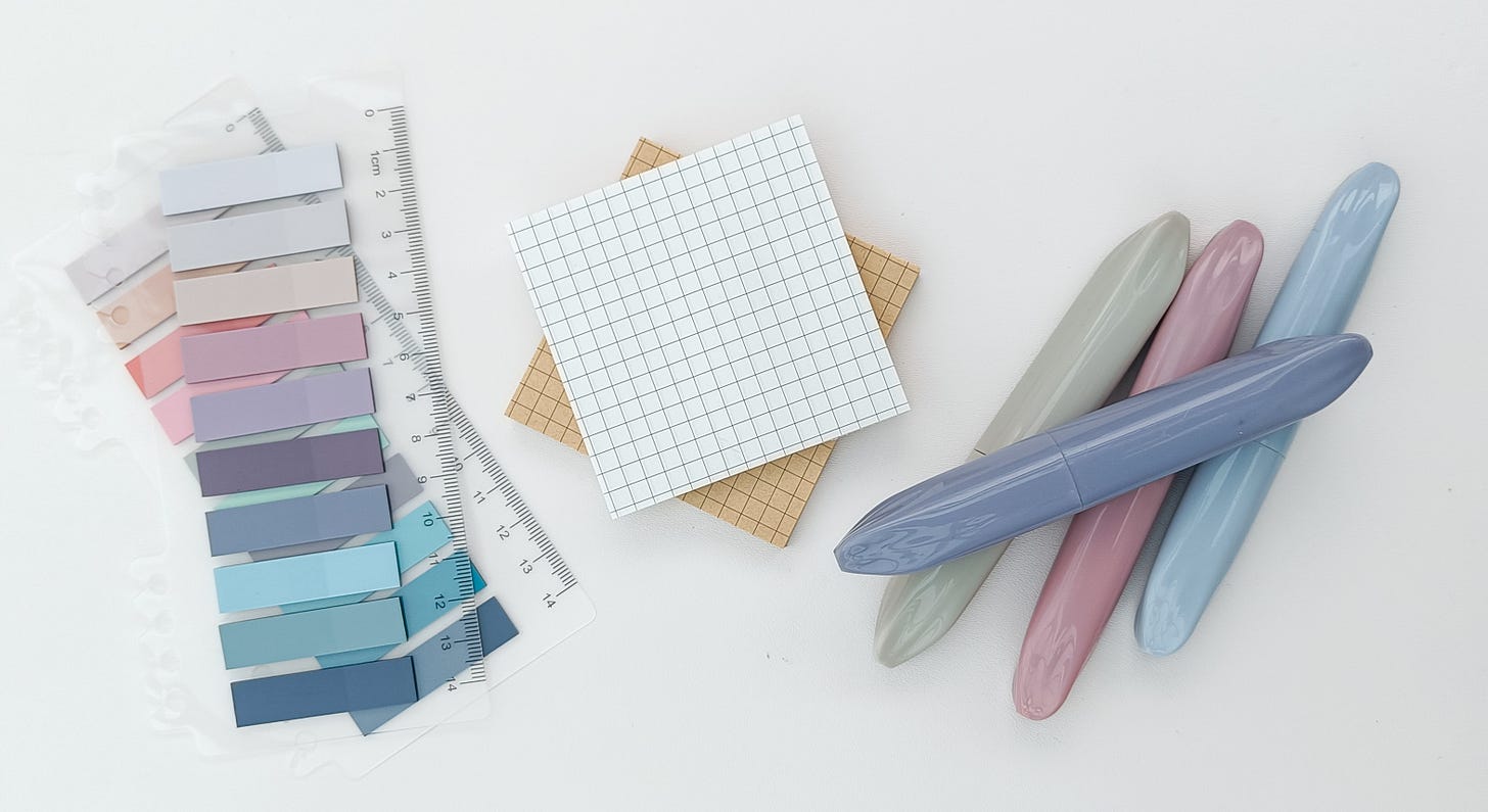 IMG: a flat lay of stationery items - transparent sticky page flags, sticky paper notes with grid, pastel highlighters.