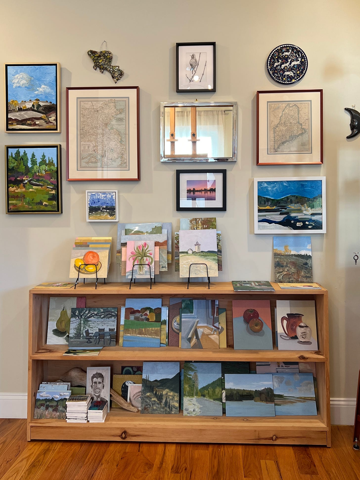 A wall with paintings and a shelf sitting on the floor with more paintings inside an artist's home studio. 