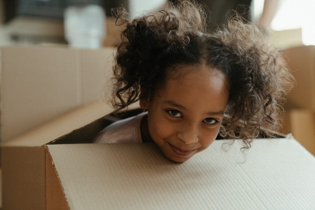 Girl in white turtleneck shirt smiling from inside a box