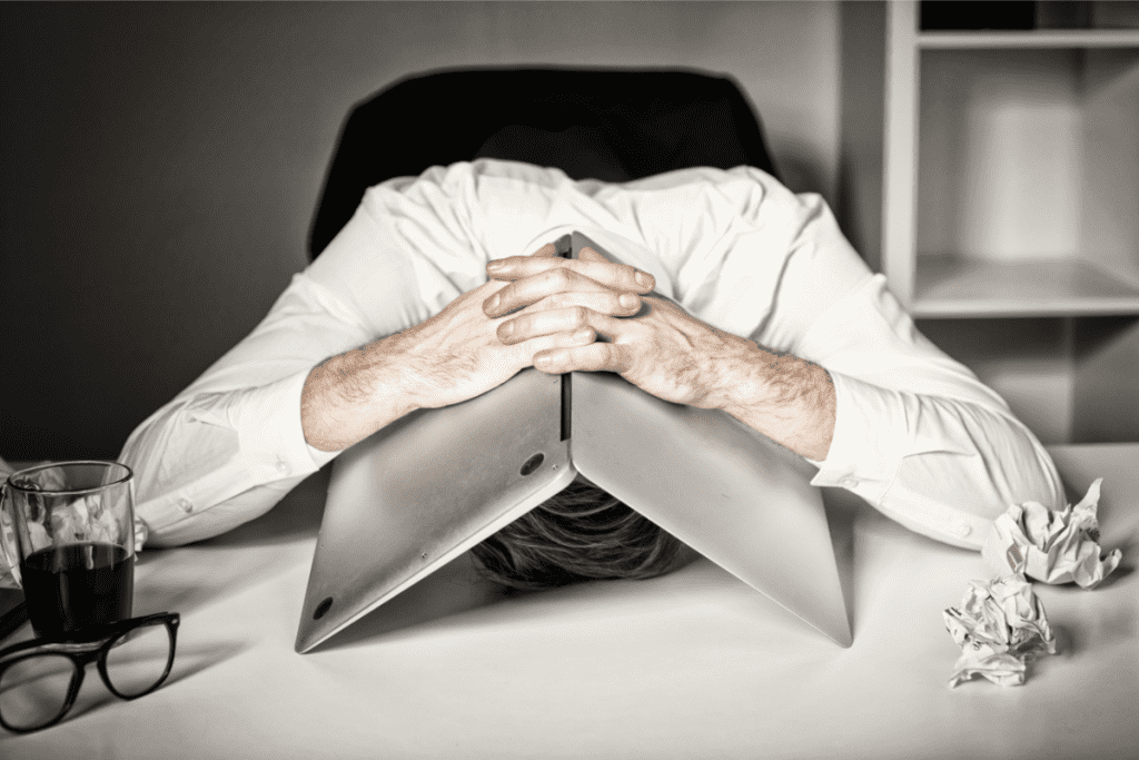 overhelmed man with head on desk under laptop needs to avoid burnout through mindfulness practices and mindful productivity