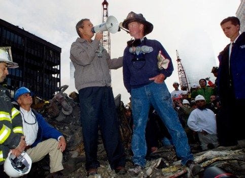 As rescue efforts continue in the rubble of the World Trade Center in New York, President Bush stands with firefighter Bob Beckwith on a burnt fire truck in front of the World Trade Center during a tour of the devastation, Friday, Sept. 14, 2001. Other people in photo are undentified. (AP Photo/Doug Mills)