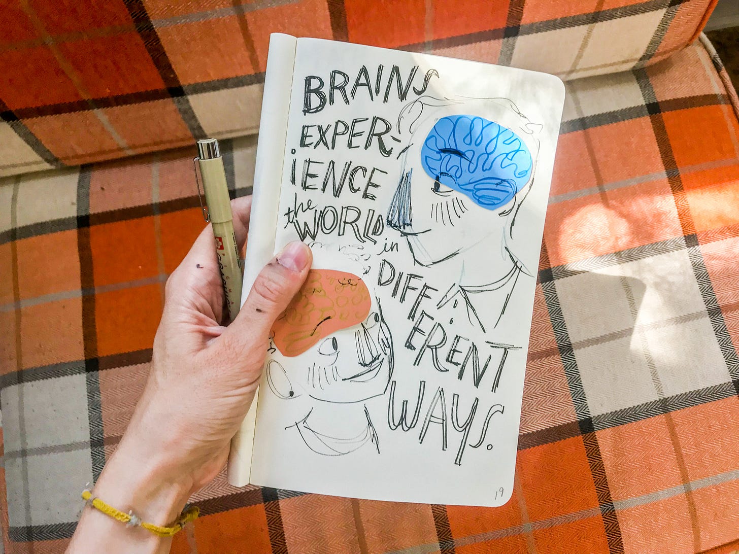 A photograph of Gracie's hand holding up her sketchbook, showing an early concept art piece with the quote "brains experience the world in different ways."