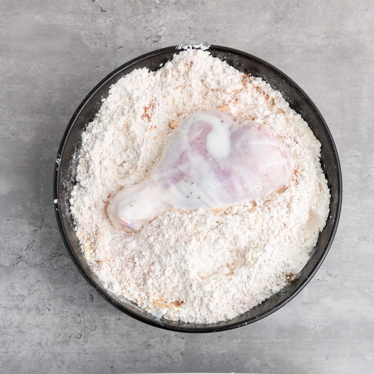 Buttermilk-coated chicken drumstick sitting on top of a bowl of flour.