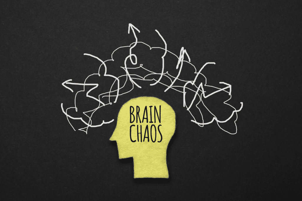 brain chaos written in black on yellow silhoutte of head on black background with white sribbling anxiety and stress