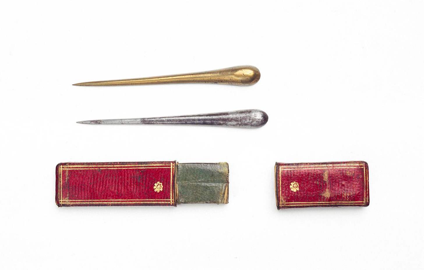 The picture shows two metal prongs, each with a pointed end and a rounded end. They appear to be made from different metals. Below them is a red leather case, in which they would have been carried.