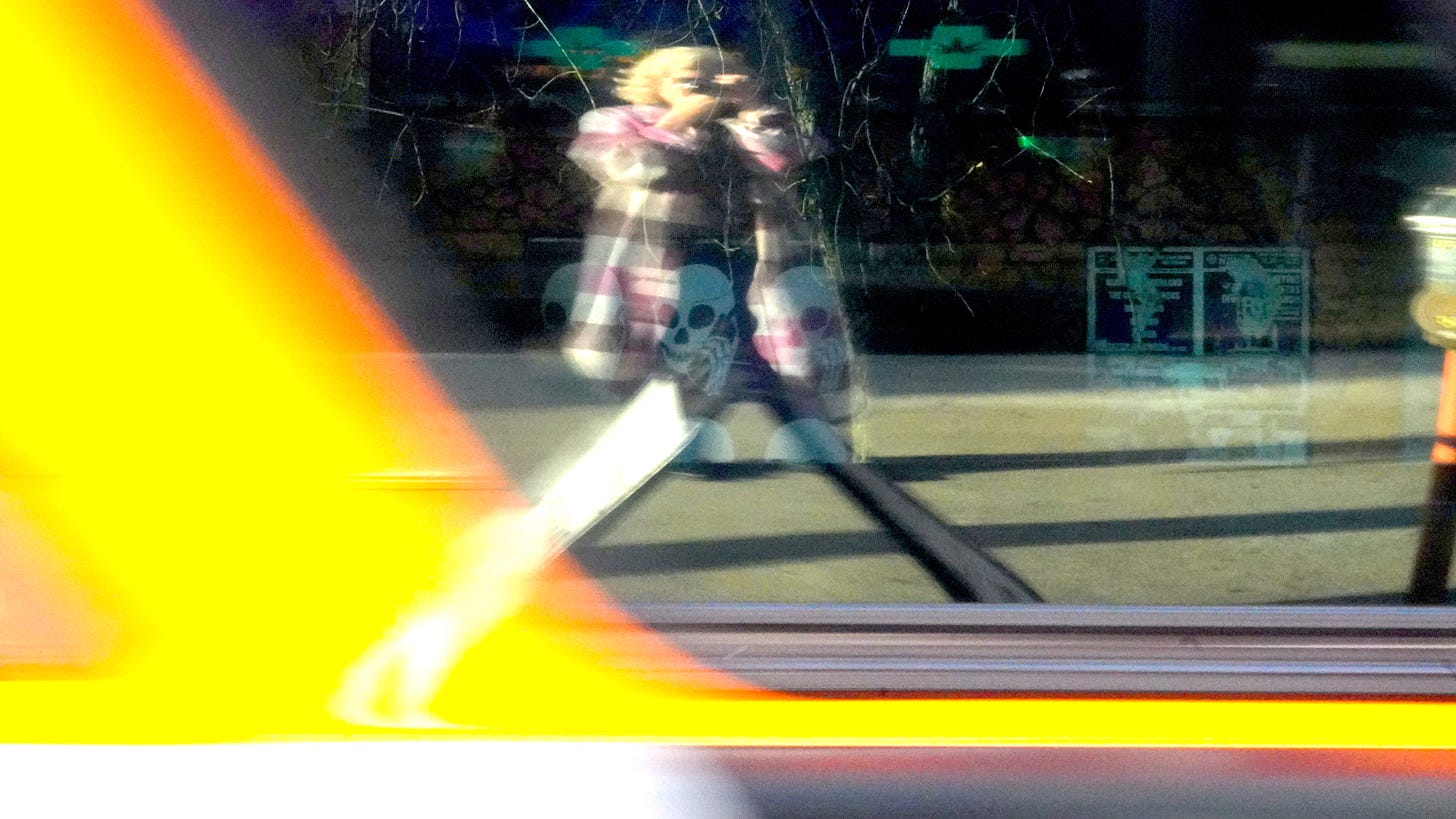 A blonde woman in a pink plaid coat as seen in the blurred reflection of a passing bus.