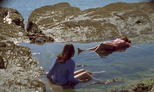 Two women laying in a water pool near the sea