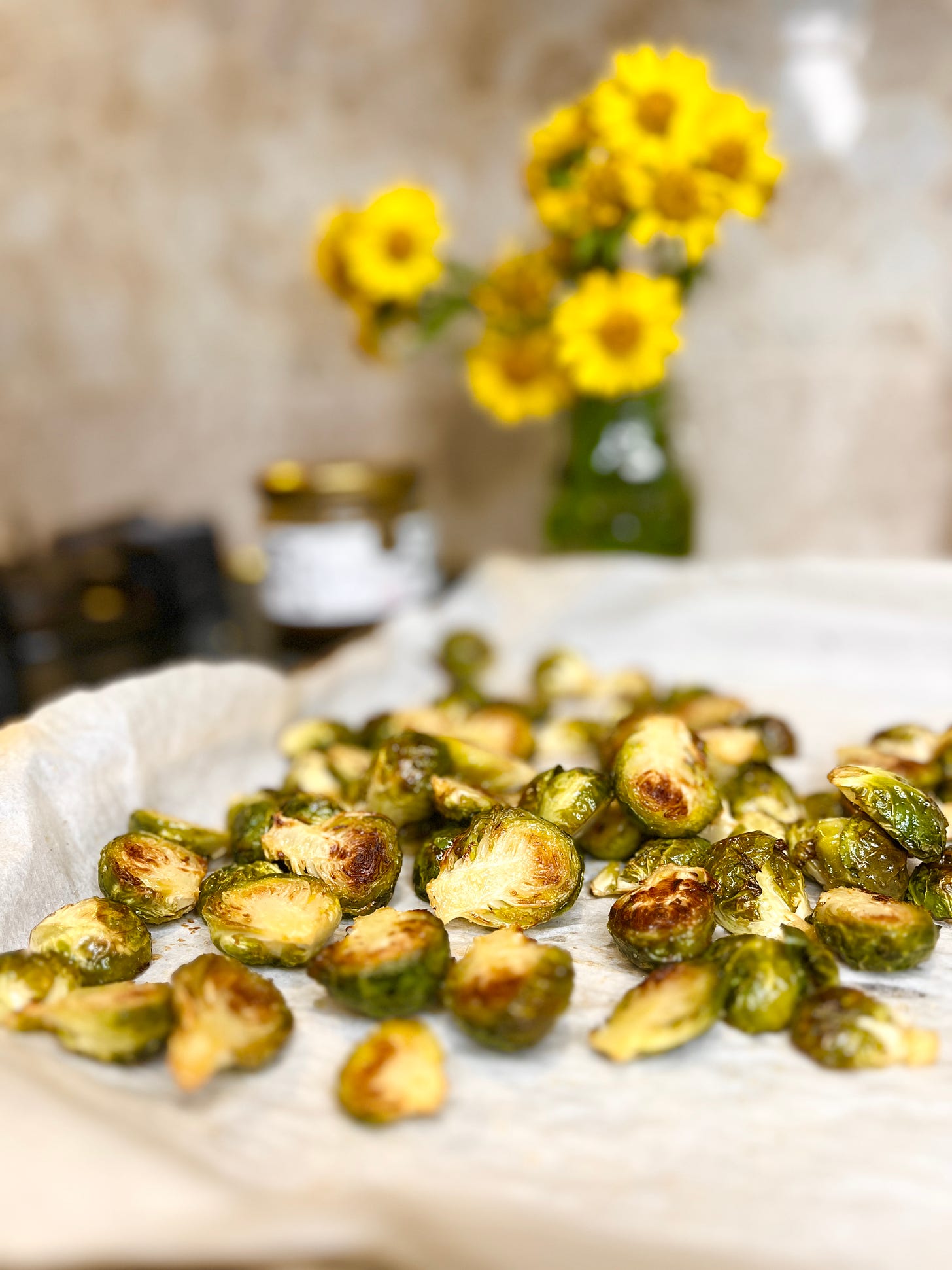 roasted brussels sprouts on a parchment lined baking sheet, with a jar of yellow wildflowers and a jar of honey in the background