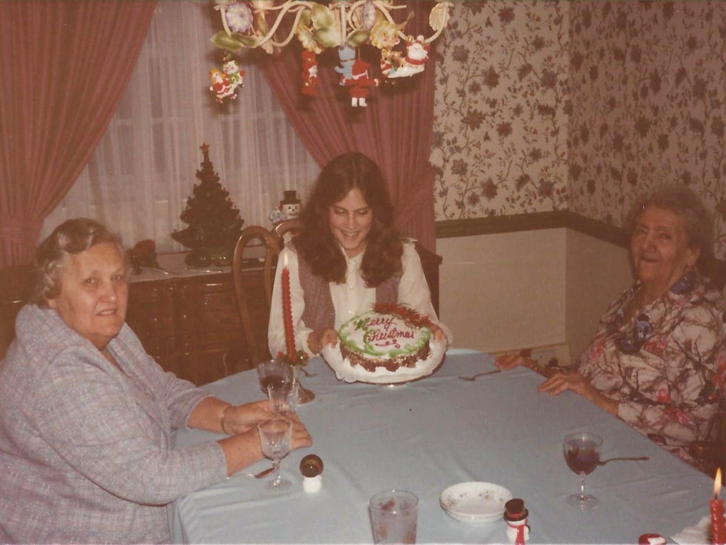Two grandmoms look on as their granddaughter displays a lavishly decorated Merry Christmas cake
